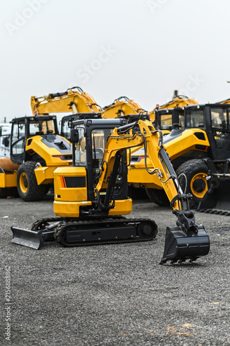 Mini excavator and other construction machinery parked in an equipment yard. Heavy equipment ready for work, transport, or use at construction and infrastructure sites.