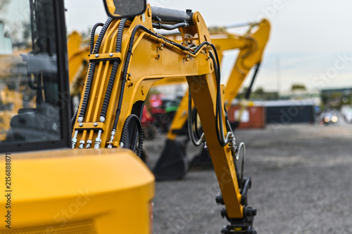 Mini excavator and other construction machinery parked in an equipment yard. Heavy equipment ready for work, transport, or use at construction and infrastructure sites.