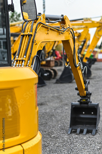 Mini excavator and other construction machinery parked in an equipment yard. Heavy equipment ready for work, transport, or use at construction and infrastructure sites.