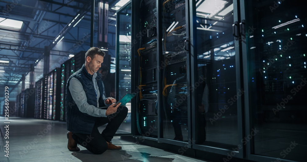 Fototapeta premium Caucasian Male Network Engineer Kneeling on Floor Beside Server Rack Cabinet, Using Laptop Computer for System Maintenance and Performance Monitoring in Modern AI Data Center Facility