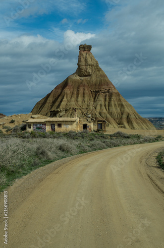A dirt road and an adobe house with graffiti in front of the Castildetierra, semi-desert Bardenas Reales, Spain, portrait format