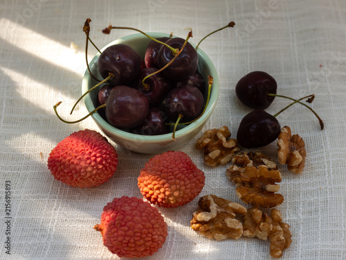 Quadro su tela Ripe dark sweet cherries, Prunus avium, fresh lychee, Litchi chinensis, and walnut kernels, Juglans regia, arranged on natural linen