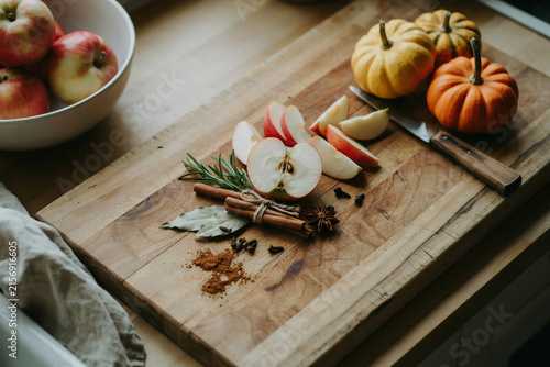 Rustic autumn food preparation with sliced apples and pumpkins on wooden board. Seasonal harvest ingredients with cinnamon and spices.
