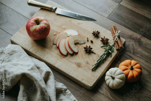 Rustic autumn food preparation on wooden cutting board. Sliced red apples with cinnamon sticks and star anise. Seasonal fall ingredients.