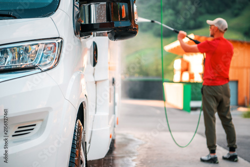 Принти на полотні Man washes a white van at a car wash near a green hillside
