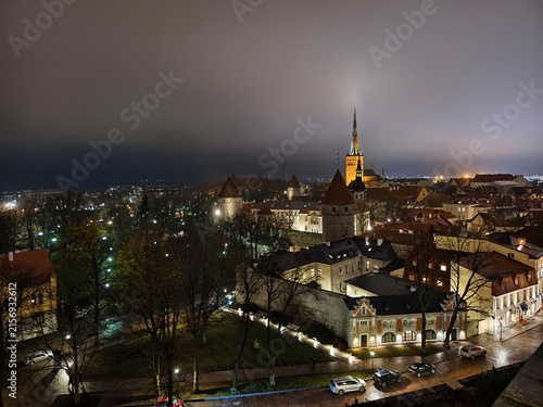 High angle wide view of illuminated Tallinn Old Town skyline at night with medieval city wall towers and St. Olaf's Church spire in Estonia