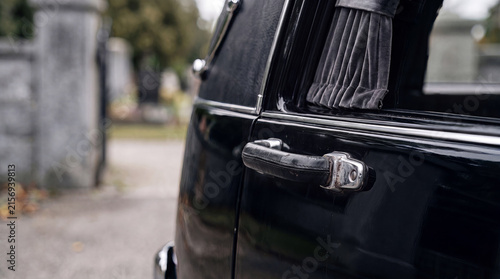 Close-up of a black vintage hearse door with velvet curtains near a cemetery