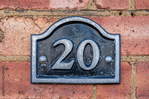 Vintage style metal house number 20 plaque mounted on a traditional red brick wall.