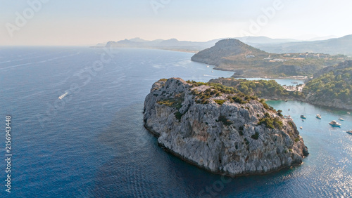 Rocky islet with white cliffs surrounded by deep blue sea near a hazy coast