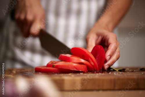 Chef slicing fresh tomato on wooden board