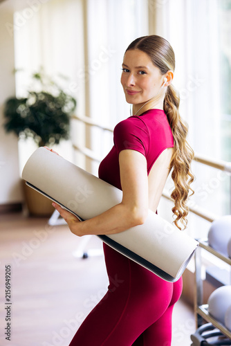 Healthy young woman in sportswear carrying a pilates mat while preparing for a fitness workout in a modern gym