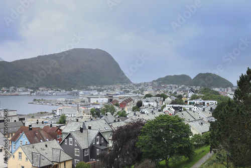 Traditional coastal houses and harbor in Alesund town, Norway. Scandinavian cityscape with ocean bay, mountains under dramatic sky.