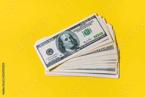 Stack of hundred dollar bills on bright yellow background