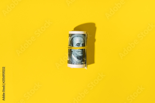 Roll of hundred dollar bills on yellow background