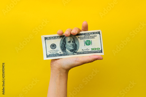 Hand holding hundred dollar bills on yellow background