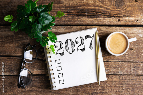 New year resolutions 2027 on desk. 2027 goals list with notebook, coffee cup, plant on wooden table. Resolutions, plan, goals, action, checklist, idea concept. New Year 2027 resolutions, copy space