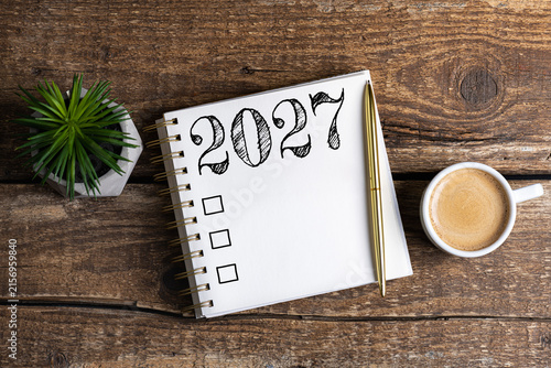New year resolutions 2027 on desk. 2027 goals list with notebook, coffee cup, plant on wooden table. Resolutions, plan, goals, action, checklist, idea concept. New Year 2027 resolutions, copy space