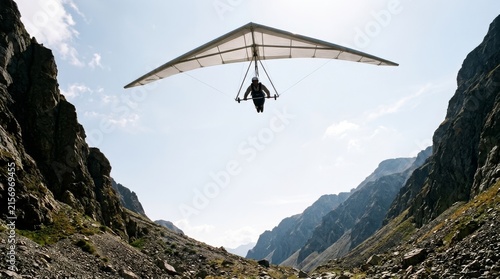 A person glides with a hang glider between tall rocky canyon walls.