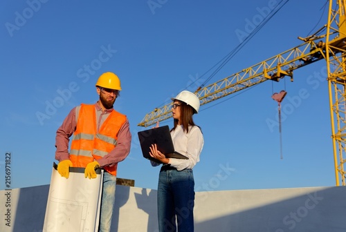 Construction workers discussing blueprint on building site with crane