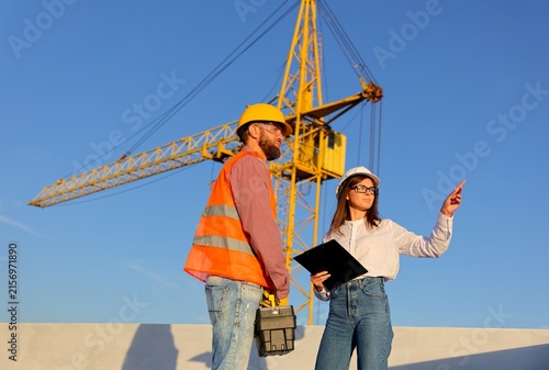 Construction manager and engineer discussing building project on site with crane in background