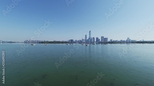 A wide urban lake with small boats, flanked by modern skyscrapers under a clear bright blue sky on a calm day.