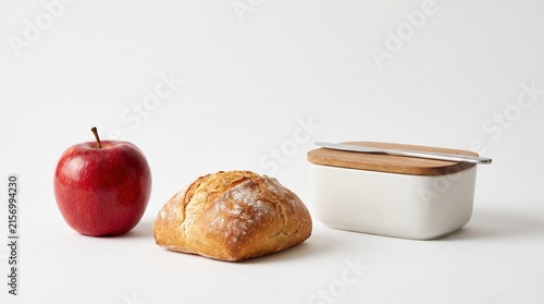 Fresh Food Arrangement with Red Apple, Bread, and White Container on Neutral Background