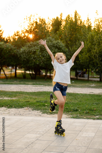 A joyful girl poses in the park on one roller skate with her arms raised