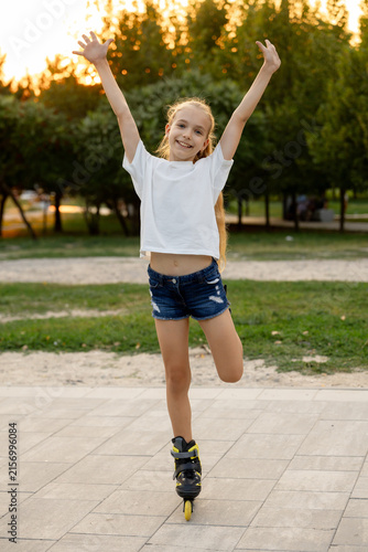 A joyful girl poses in the park on one roller skate with her arms raised
