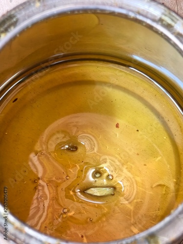 Close-up of golden yellow liquid with small bubbles and debris inside a metal can