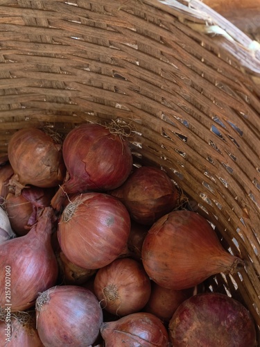 A woven basket filled with numerous red and brown onions, their dry skins and roots visible, creating a rustic food display