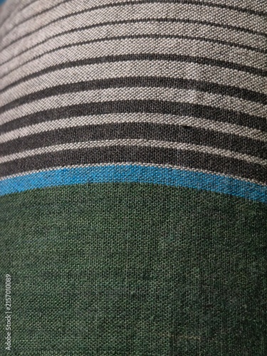 Close-up abstract view of a woven textile with horizontal stripes of gray black and blue on a dark green fabric