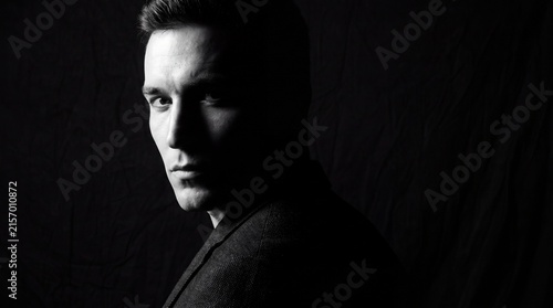 Dramatic black and white portrait of a serious young man in shadow with moody monochrome portrait man side lighting against dark background