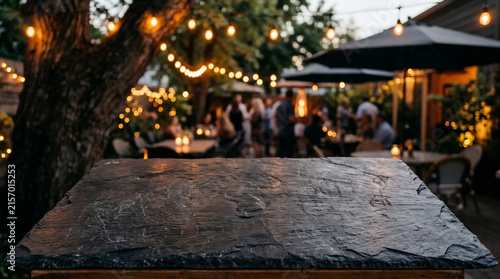 Rough slate tabletop with blurred outdoor restaurant at dusk with string lights and people, suitable for food advertising, restaurant marketing and lifestyle photography