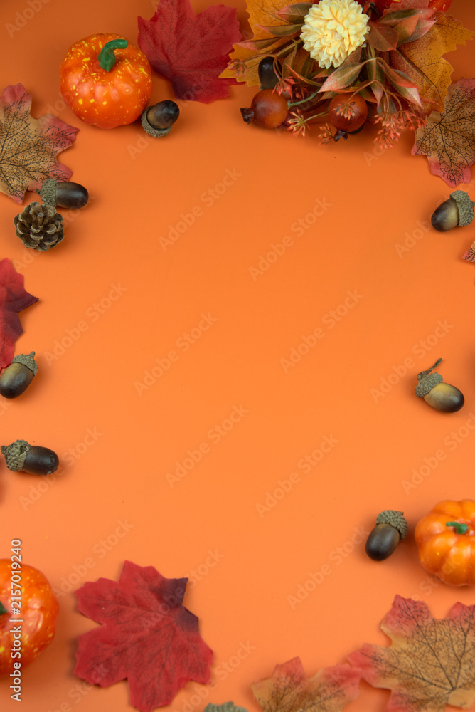 Obraz premium Autumn decorative elements like pumpkins, leaves, and acorns forming a frame on an orange background, perfect for copy space