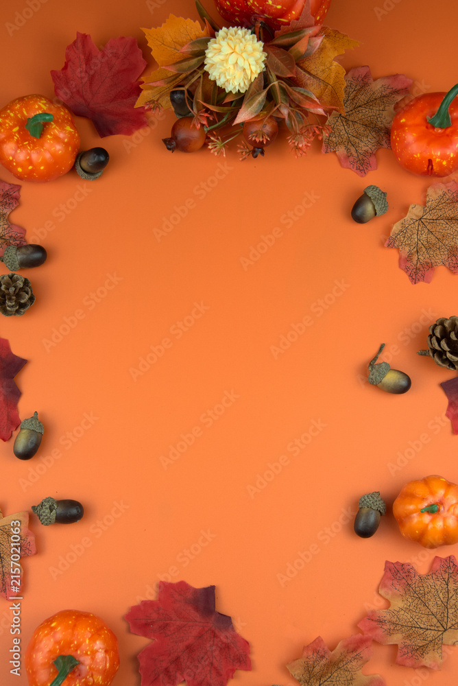 Fototapeta premium Fall decoration with pumpkins, leaves, and acorns framing a vibrant orange background, perfect for seasonal designs