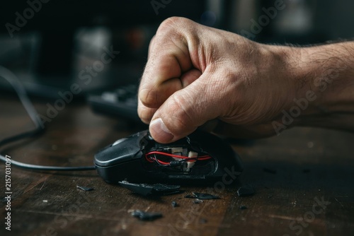 Fist smashing a broken computer mouse on a wooden desk, frustration and anger concept