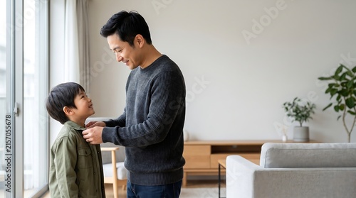 A father gently adjusts his young son s jacket while standing near a window in a modern living room affection