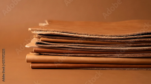 Stack of high quality brown leather sheets showing rustic textures and natural edges photographed against a matching solid color background