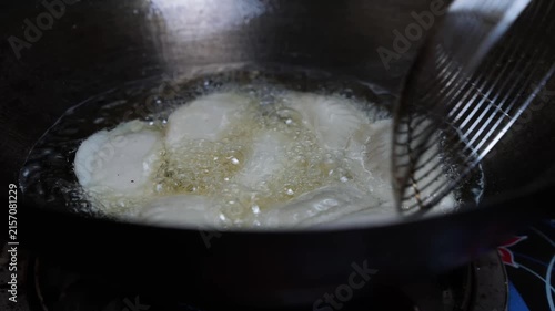 Close up of food frying in hot oil in a dark pan with bubbles and a metal skimmer, showing cooking in the kitchen