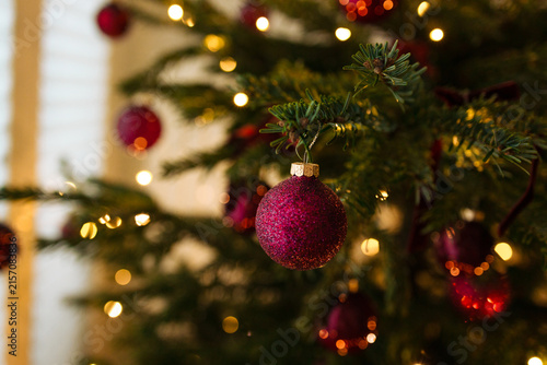 Beautiful vertical video of a shiny purple bauble decorating a green Christmas tree with magical shimmering golden fairy lights in the background.