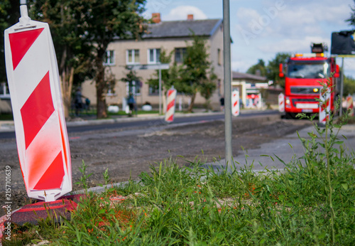Red and white warning barricade at a residential street construction site with a dump truck
