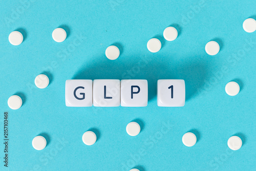 GLP 1 word on blocks surrounded by medicine pills on blue background