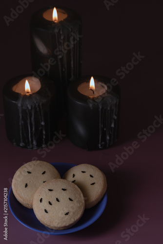 Halloween sugar cookies with bat sprinkles on blue plate accompanied by burning black pillar candles on purple backdrop with copy space for party menu promotion