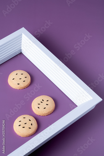 Creative geometric arrangement featuring Halloween cookies with black bat framed inside a white picture frame on a purple background, creating copy space for seasonal promo layouts