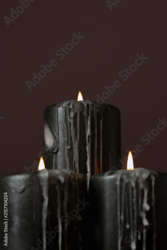 Three burning black pillar candles with wax drips on dark purple background creating spooky atmospheric lighting for Halloween celebration and gothic decor