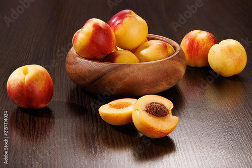 Ripe nectarines in a wooden bowl with a halved fruit showing its pit