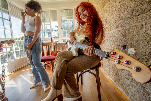 Foto Two young women rehearse music indoors, with red haired bassist seated and smili