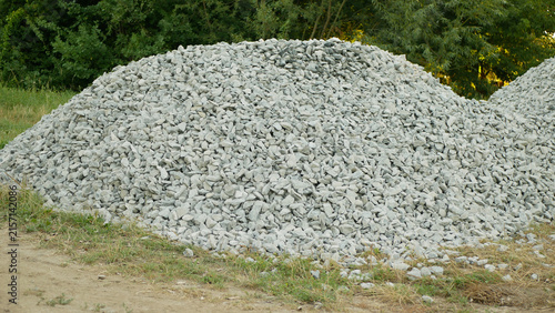Macadam crushed stone gravel aggregate angular rocks granite, basalt, construction of roads, highways and houses, limestone gravel mound shaped heap light gray macadam stone piled layered patch trees