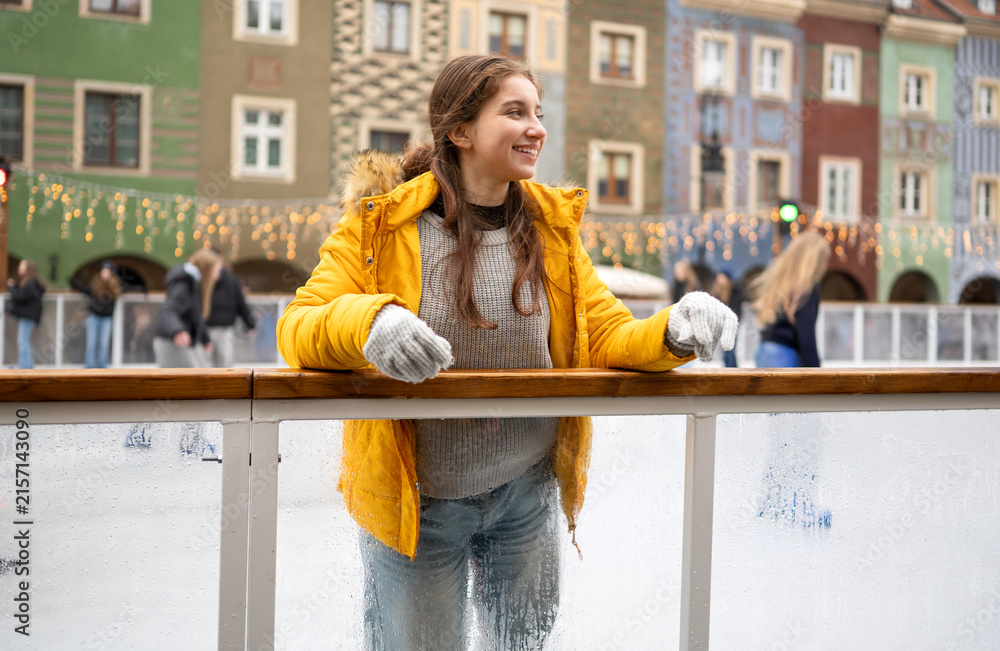Fototapeta premium Happy teenager rests on railing near ice rink in Poznan market square during cold winter daylight