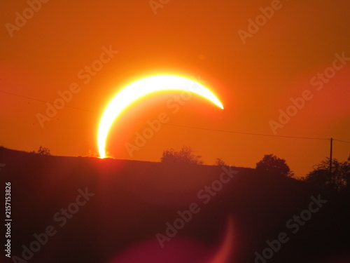 фотографія A brilliant solar eclipse creates a glowing crescent sun over the silhouetted hills of Mioglia, Italy, during a warm summer sunset